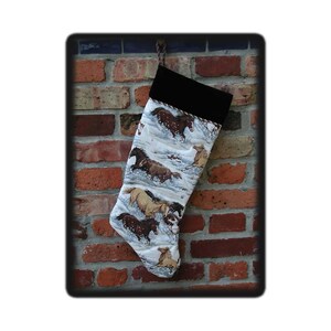 May include: A Christmas stocking with a black cuff and a fabric body featuring a winter scene with running horses. The stocking is hanging against a brick wall. The text "#1328 rrdesigns561.etsy.com" is visible.
