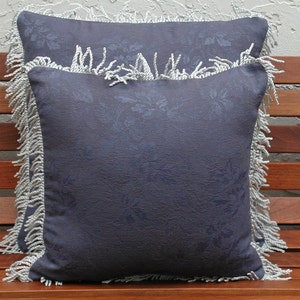 May include: Two decorative throw pillows with a dark blue fabric and a white floral pattern. The pillows have a white fringe trim.