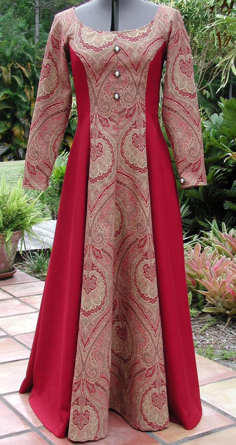 May include: A long-sleeved red dress with a paisley pattern in gold and red. The dress has a scoop neckline and a fitted bodice. The skirt is full and flowing.