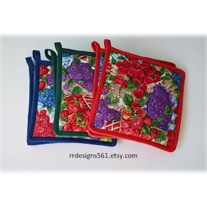 May include: Three square fabric pot holders featuring a vibrant fruit print with strawberries, cherries, and grapes. Each pot holder has a solid colored fabric border in blue, green, or red, and includes a small fabric loop for hanging.