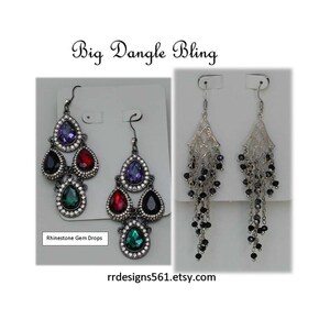 May include: Two pairs of dangle earrings labeled Big Dangle Bling and Rhinestone Gem Drops. The left pair features multi-colored teardrop gems in dark metal settings. The right pair consists of silver-toned chain tassels with small black beads.