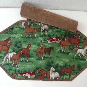 May include: A green and brown table runner with a horse design. The runner is made of fabric and has a brown border. The runner is shaped like a hexagon.