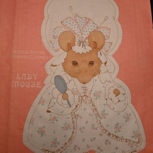May include: A vintage sewing pattern for a Lady Mouse doll. The pattern features a pink background with a white mouse wearing a blue and pink dress and holding a mirror. The text "Beatrix Potter Nursery Classics" and "Lady Mouse" is printed on the pattern.