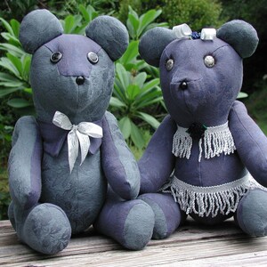 May include: Two plush gray teddy bears with white accents. One bear has a white bow tie and the other has a white beaded necklace and skirt.