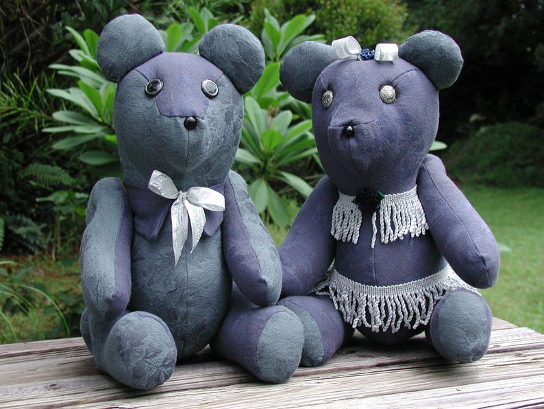 May include: Two plush gray teddy bears with white accents. One bear has a white bow tie and the other has a white beaded necklace and skirt.
