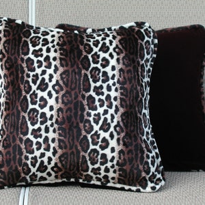 Pode incluir: Duas almofadas decorativas, uma com estampa de leopardo marrom e branco e a outra com tecido marrom escuro sólido. Ambas as almofadas têm uma borda branca.