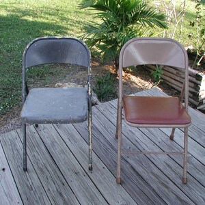 May include: Two folding chairs, one with a gray metal seat and back, the other with a brown vinyl seat and a beige metal frame. Both chairs are on a wooden deck.