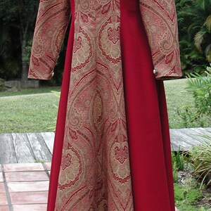 May include: A long-sleeved red and gold dress with a paisley pattern. The dress has a scoop neckline and is fitted at the waist. The dress is made of a soft, flowing fabric.
