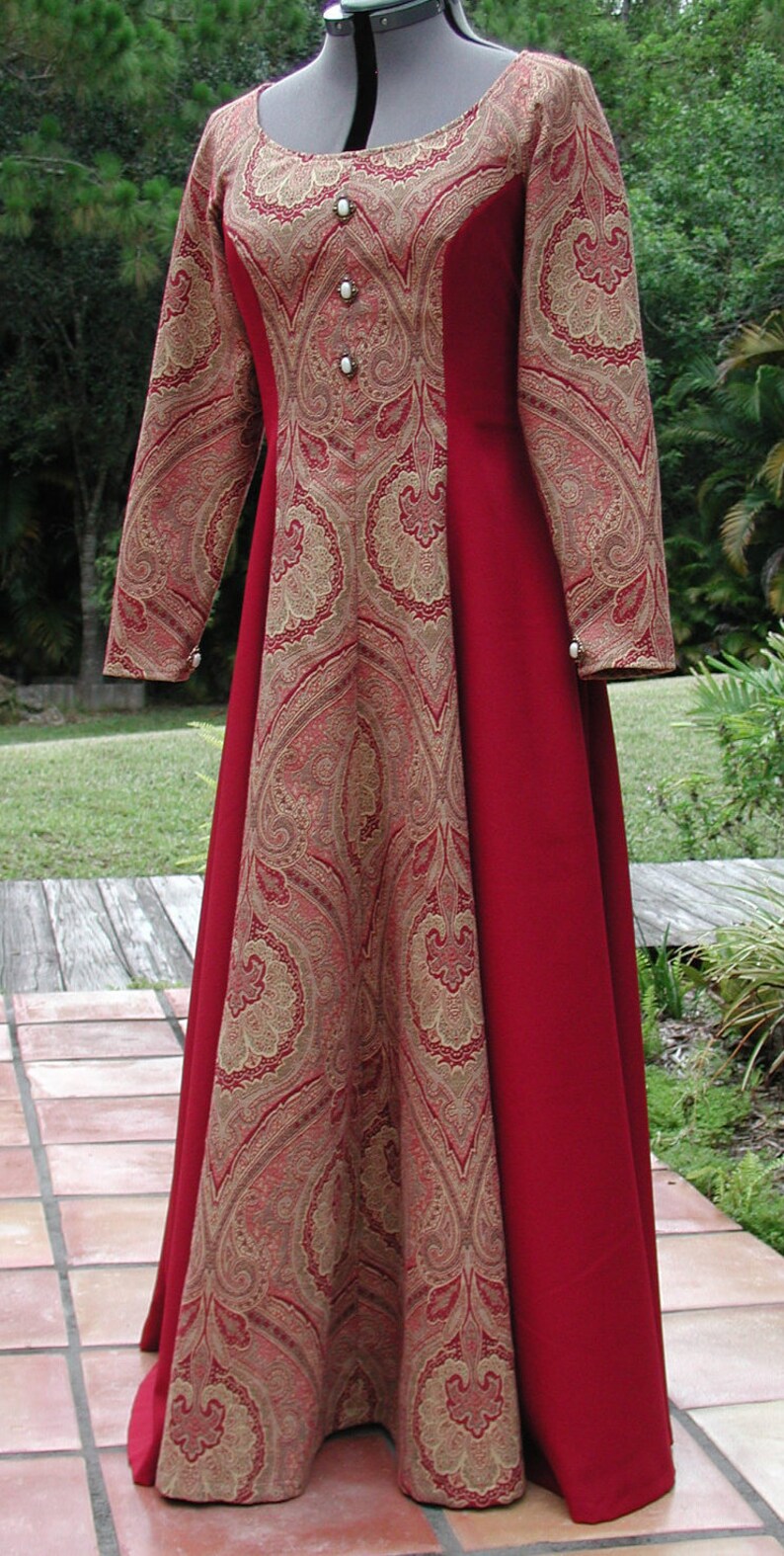 May include: A long-sleeved red and gold dress with a paisley pattern. The dress has a scoop neckline and is fitted at the waist. The dress is made of a soft, flowing fabric.