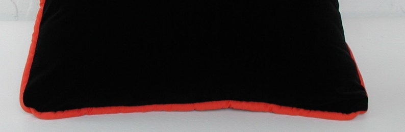 K&ouml;nnte beinhalten: Schwarzes Samtkissen mit einem leuchtend orangenen Rand.