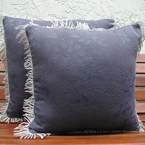 May include: Two decorative throw pillows with a dark blue floral pattern and white fringe trim.