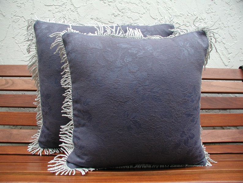 May include: Two decorative throw pillows with a dark blue floral pattern and white fringe trim.