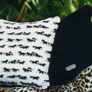 May include: Two square throw pillows, one featuring a white fabric with a repeating pattern of black running horses, and the other a solid black fabric. A small rectangular white label with red and blue text is attached to the black pillow.