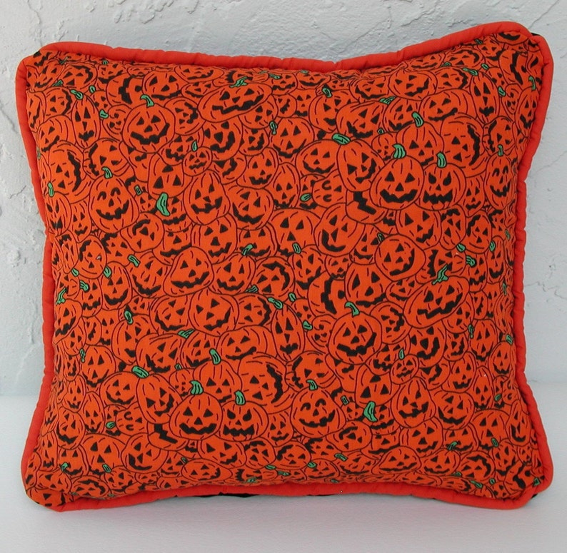 K&ouml;nnte beinhalten: Orangefarbener Kissenbezug mit Halloween-Motiv, das ein sich wiederholendes Muster aus schwarzen K&uuml;rbisgesichtern zeigt.