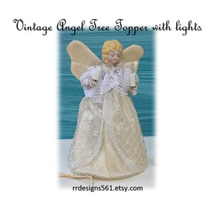 May include: An angel tree topper with blonde hair, cream-colored wings, and a white lace dress. The figure holds two small white electric candles. The text reads: Vintage Angel Tree Topper with lights and rrdesigns561.etsy.com.