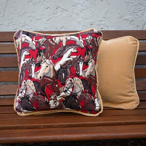May include: Two decorative throw pillows on a wooden bench. One pillow is a solid beige color, and the other has a red background with a repeating pattern of horse heads in various colors.