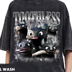 Puede incluir: Camiseta negra con lavado mineral con un gráfico de Chimuelo de Cómo entrenar a tu dragón. El diseño incluye múltiples personajes de Chimuelo, rayos y la palabra "TOOTHLESS" en plata.