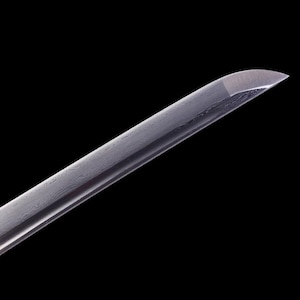 May include: Close-up of the tip of a silver katana sword blade, showing the intricate pattern of the steel.
