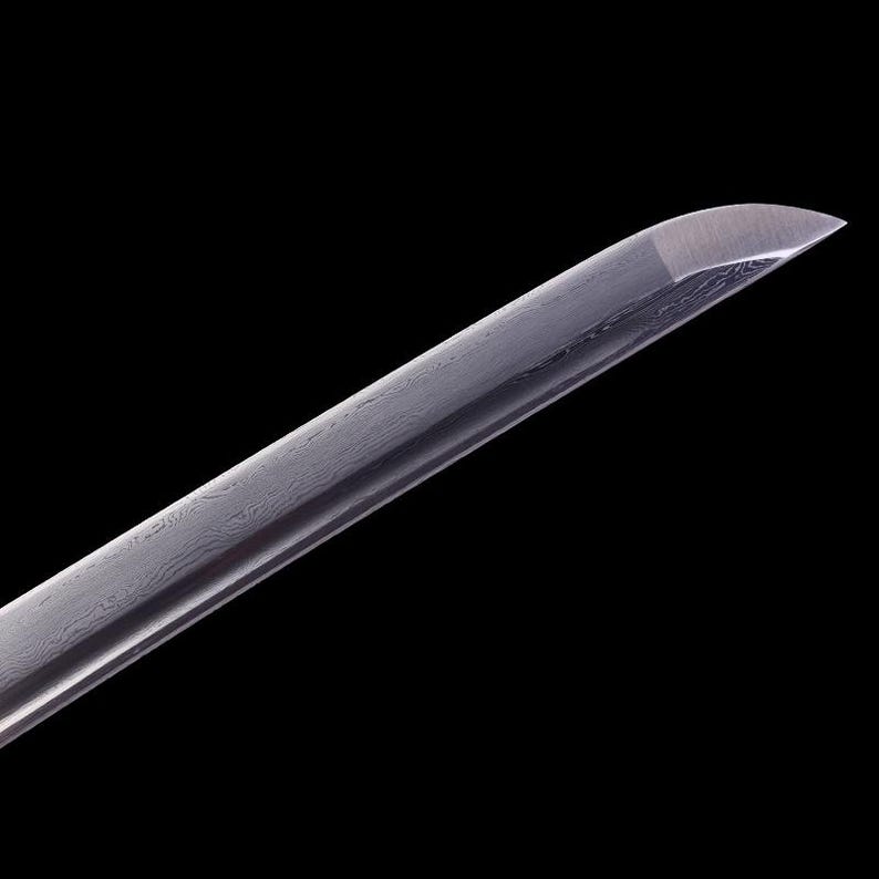 May include: Close-up of the tip of a silver katana sword blade, showing the intricate pattern of the steel.