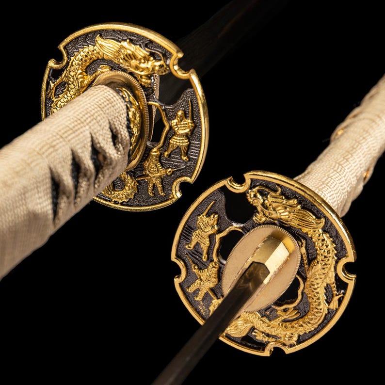 May include: Close-up of a Japanese katana sword. The sword features a gold dragon and warrior design on the handguard. The handle is wrapped in a cream fabric. The blade is black.