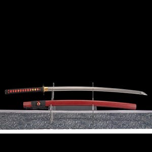 Peut inclure: Un katana japonais avec un manche rouge et noir et une lame argent&eacute;e, expos&eacute; sur un support transparent. Le fourreau rouge est en dessous de la lame. Le fond est noir.
