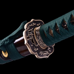 May include: Close-up of a green and gold katana sword with a decorative metal tsuba, or hand guard, featuring intricate floral and dragon designs.