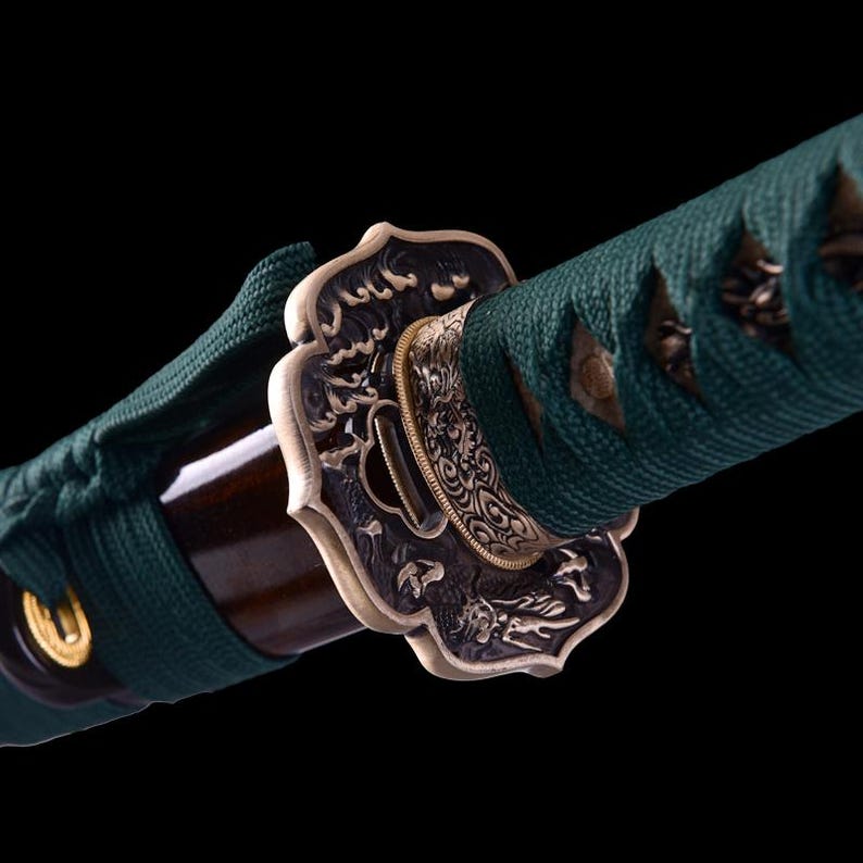 May include: Close-up of a green and gold katana sword with a decorative metal tsuba, or hand guard, featuring intricate floral and dragon designs.