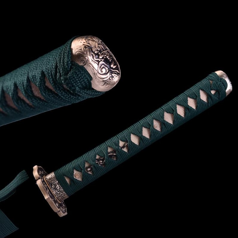 May include: A green and white katana sword with a decorative handle. The handle is wrapped in green cord and has a silver metal cap with an intricate design.