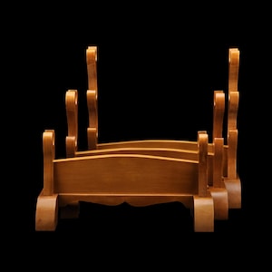 May include: Wooden sword stand with a natural finish. The stand has a tiered design with curved supports and a decorative top. The stand is designed to hold multiple swords and is set against a black background.