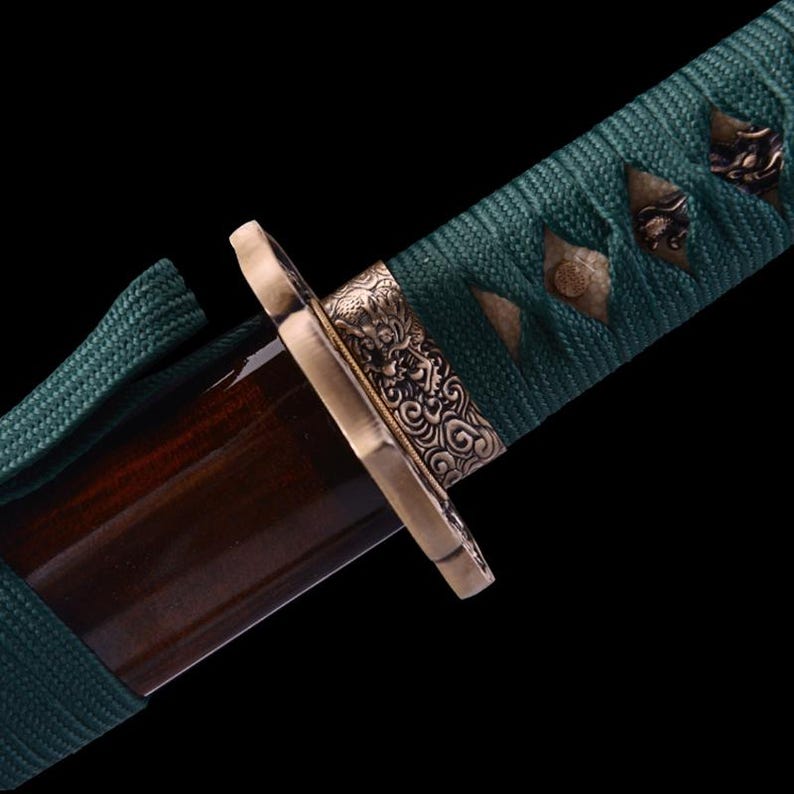 May include: Close-up of a dark brown wooden katana scabbard with a green cord wrap and a decorative brass fitting with intricate floral and dragon designs.