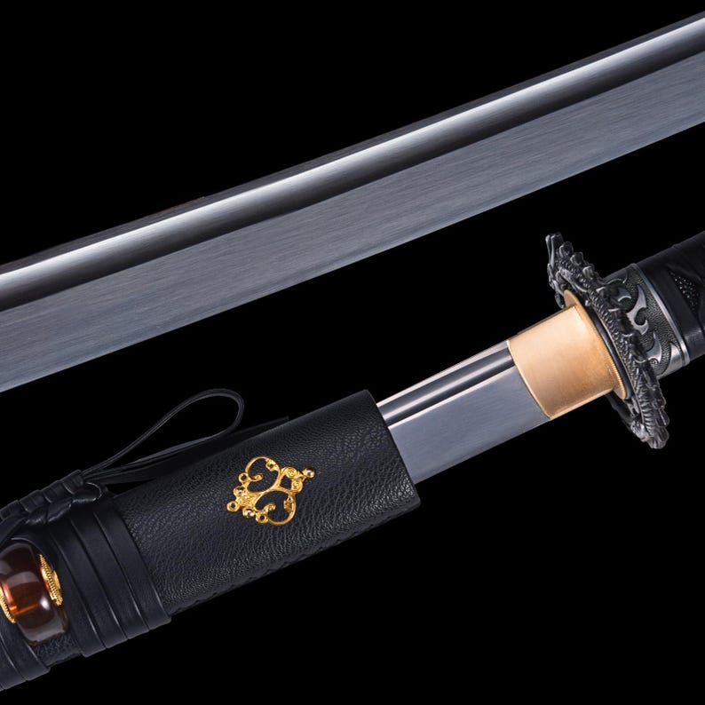May include: A Japanese katana sword with a black handle and scabbard. The blade is silver and the guard is ornate. The scabbard features a gold emblem. The sword is set against a black background.