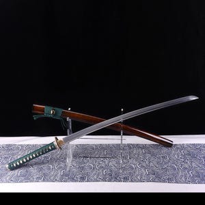 May include: A traditional Japanese katana sword with a brown wooden scabbard and a green wrapped handle. The sword is displayed on a stand with a wave pattern background.