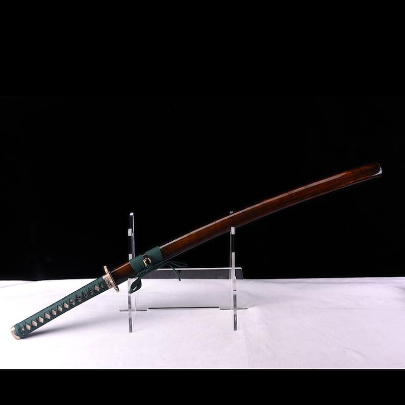 May include: A brown wooden katana sword with a green wrapped handle and a silver metal guard. The sword is displayed on a clear acrylic stand.