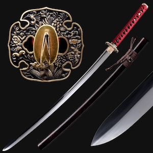 May include: A Japanese katana sword with a polished steel blade and a red handle. The sword features a decorative bronze tsuba guard with floral and leaf patterns. The scabbard is dark brown with a matching handle.