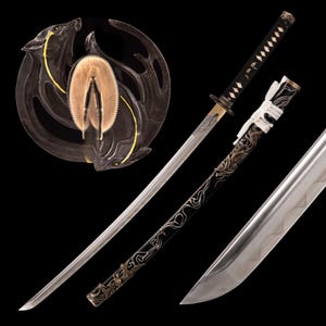 Puede incluir: Una katana japonesa con empuñadura y vaina negras, con elementos decorativos dorados y plateados. La hoja es plateada y la guarda es un diseño circular con motivos de lobos. La espada se muestra sobre un fondo negro.