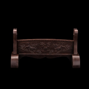 Peut inclure: Un support d'épée en bois brun foncé avec des sculptures complexes de dragons et de nuages. Le support a un dessus incurvé avec deux supports verticaux et une base avec une découpe décorative. Le fond est noir.