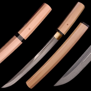 May include: Close-up of several Japanese tanto knives. The blades are silver with a curved edge, and the handles are light brown wood with black accents. The sheaths are also light brown wood. The background is black.