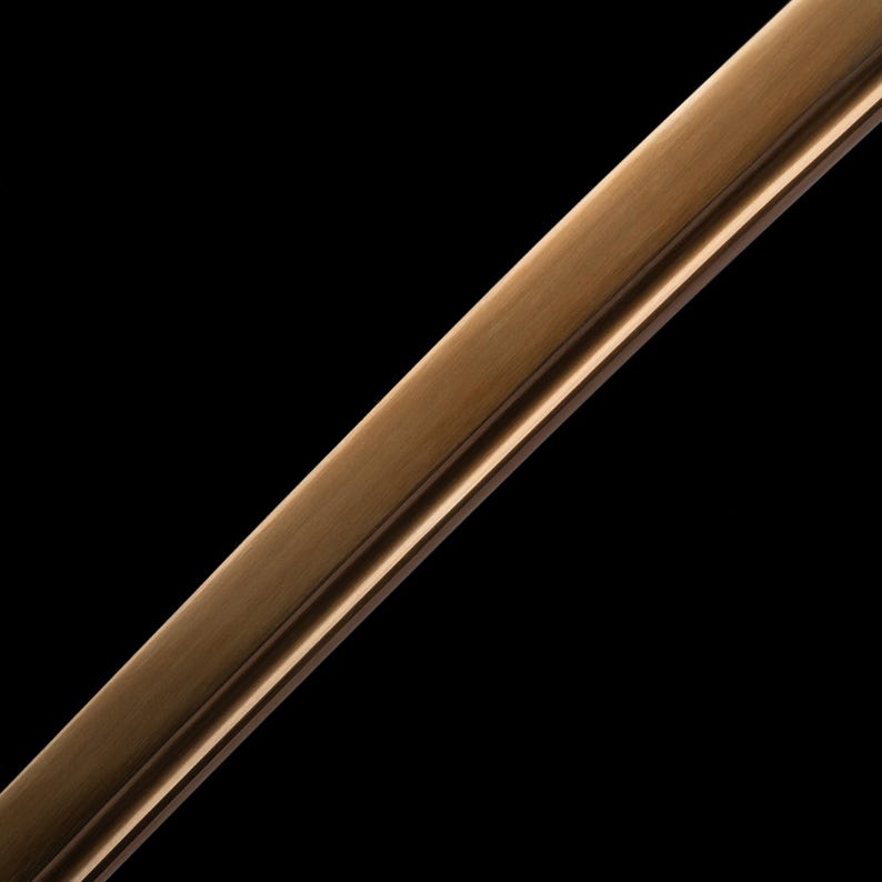 May include: Close-up of a bronze-coloured metal frame against a black background. The frame has a textured surface and a subtle, reflective sheen. The design features a raised edge and a recessed channel.