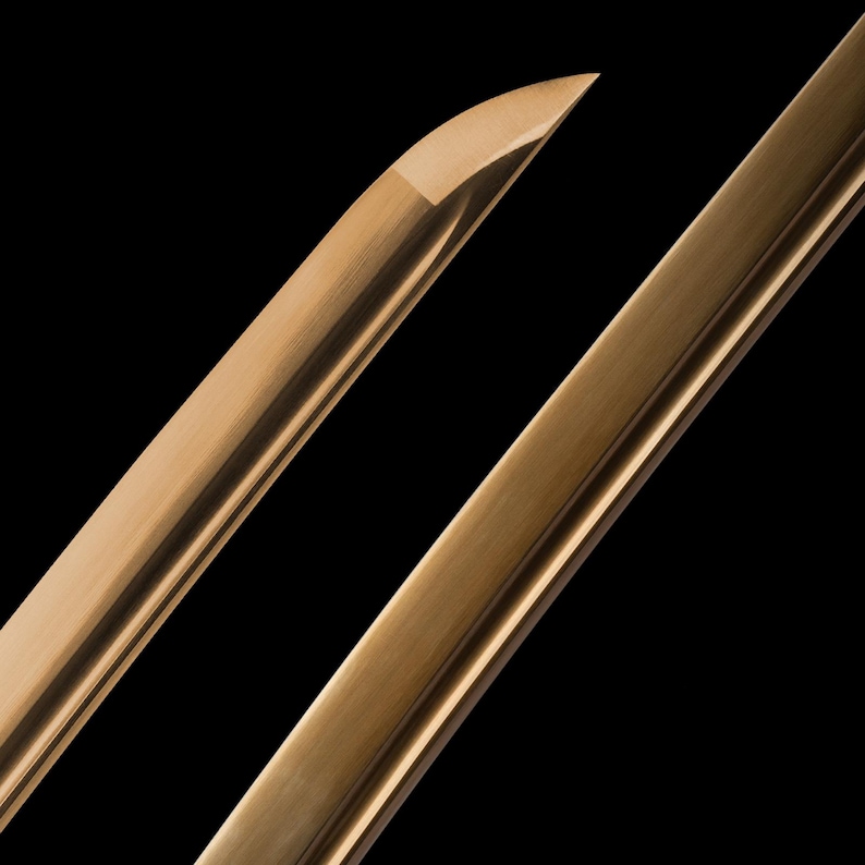 May include: Close-up of a bronze-coloured sword blade and handle against a black background. The blade has a sharp point and a polished finish. The handle is angled, showing the texture of the metal.