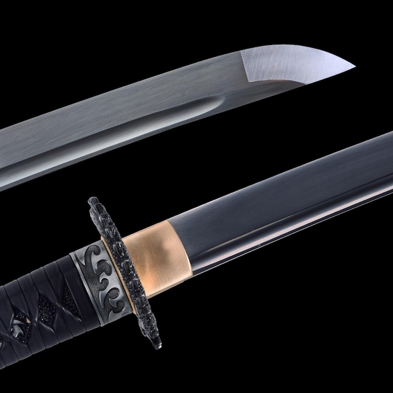 May include: Close-up of a Japanese katana sword. The blade is silver and the handle is black with intricate detailing. A gold-colored band separates the handle from the blade. The sword is set against a black background.