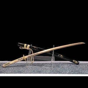 May include: A Japanese katana sword with a gold blade and a white handle. The black scabbard is decorated with gold accents. The sword is displayed on a patterned surface against a black background.