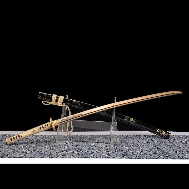 May include: A Japanese katana sword with a gold blade and a white handle. The black scabbard is decorated with gold accents. The sword is displayed on a patterned surface against a black background.