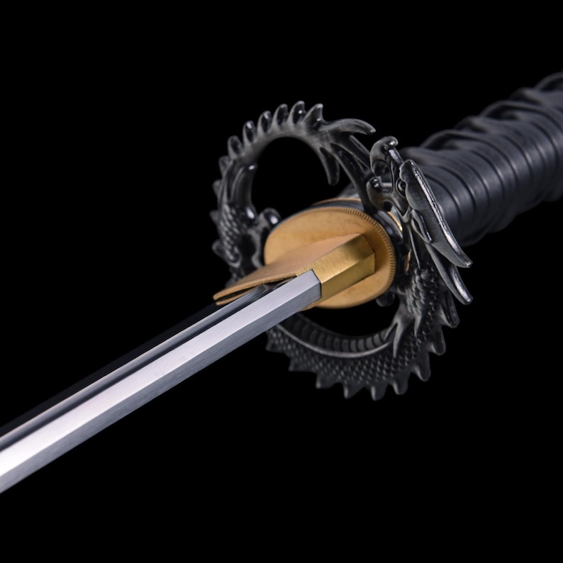 May include: Close-up of a katana sword with a silver blade and a black handle. The guard features a detailed dragon design in silver. The hilt is wrapped in black material, and the blade is sharp and reflective.