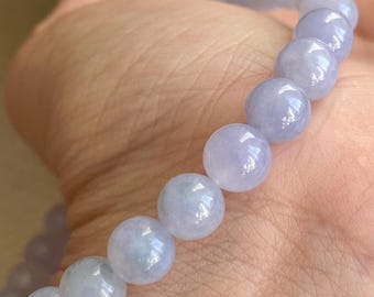May include: A beaded bracelet featuring smooth, round, light lavender-colored stones. The beads are uniform in size and have a polished, semi-translucent appearance, strung together to form a continuous circular band of light purple gemstone spheres.