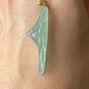 Peut inclure: Un pendentif en jade vert clair avec un motif floral. Le pendentif a une b&eacute;li&egrave;re dor&eacute;e en haut. Le jade est sculpt&eacute; d'un motif floral d&eacute;taill&eacute; et a une surface lisse et polie.