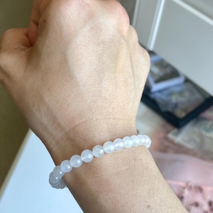 May include: A stretch bracelet composed of small, smooth, round, translucent white beads. The beads have a subtle, milky appearance and are strung together in a continuous circular loop, fitting snugly around the wrist.