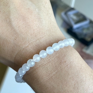 May include: A stretch bracelet composed of smooth, round, translucent white beads. The beads have a subtle, milky appearance and are strung together in a single continuous loop, creating a simple and uniform circular design around the wrist.