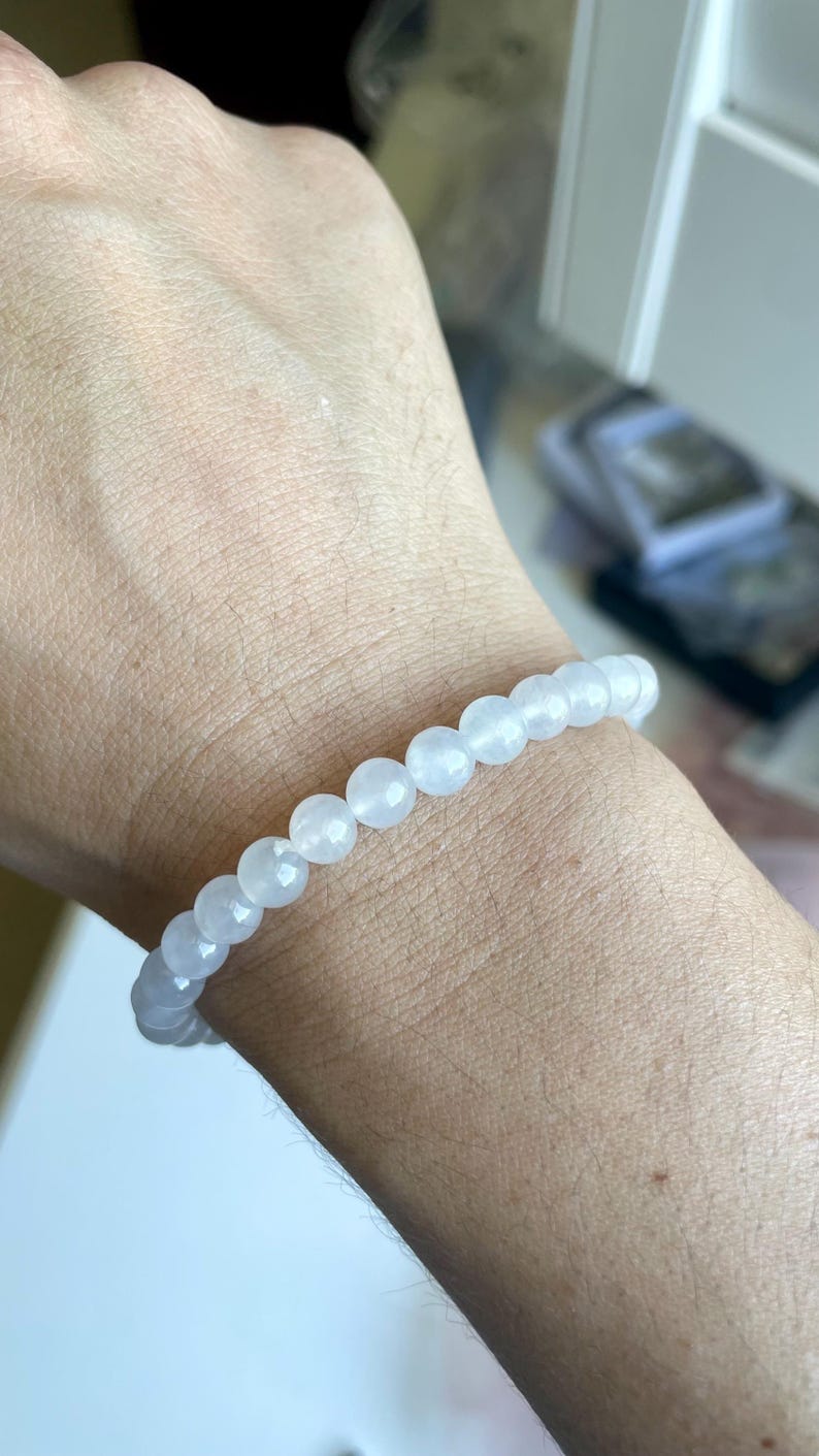 May include: A stretch bracelet composed of smooth, round, translucent white beads. The beads have a subtle, milky appearance and are strung together in a single continuous loop, creating a simple and uniform circular design around the wrist.