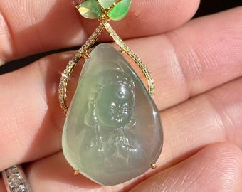 May include: A jade pendant with a carved figure, featuring a gold setting with small diamonds and three green leaf accents. The pendant is a teardrop shape and has a light green hue.