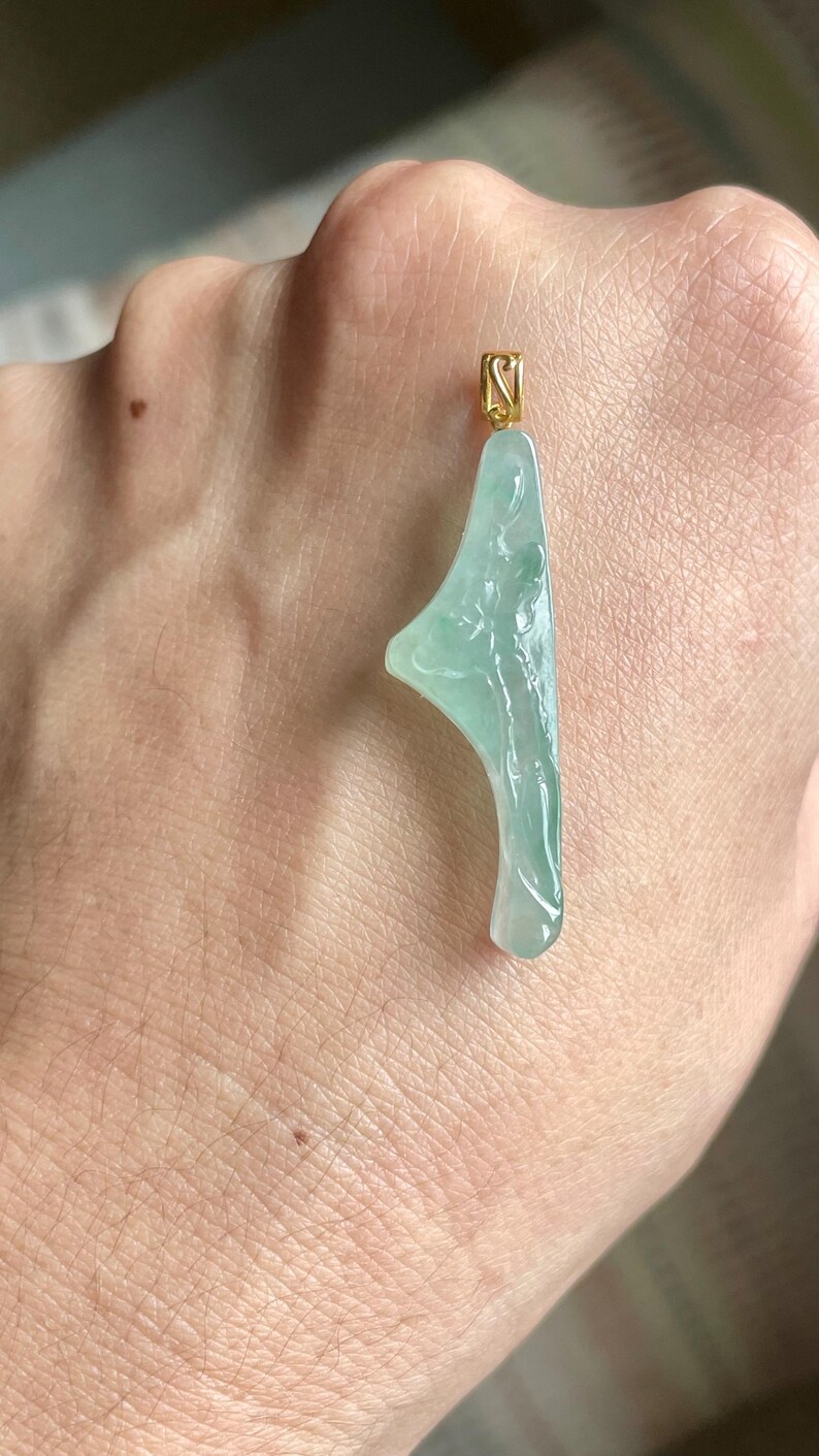 Peut inclure: Un pendentif en jade vert clair avec une b&eacute;li&egrave;re dor&eacute;e. Le jade est sculpt&eacute; dans une forme abstraite avec une surface lisse et polie. Le pendentif est suspendu par une b&eacute;li&egrave;re dor&eacute;e.
